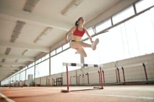 Woman in Red Sports Bra Jumping on White and Black Obstacle, marathon training