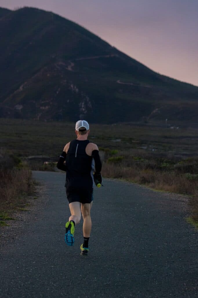 woman jogging on gray road across mountain during daytime, trail running shoes