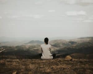 woman sitting on cliff overlooking mountains during daytime