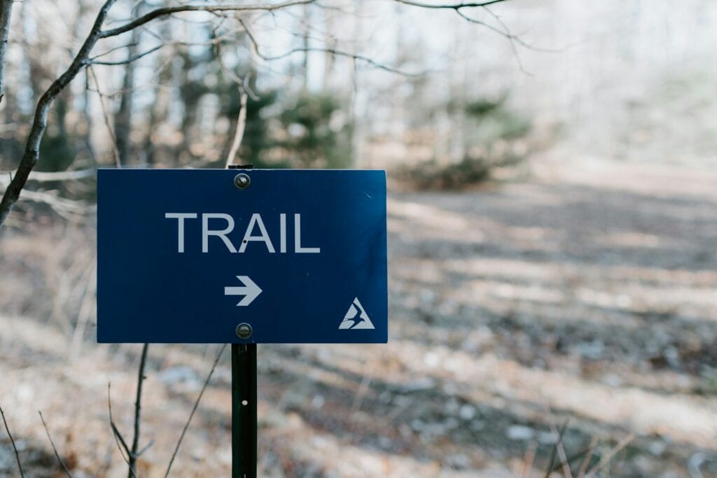 a blue sign pointing to a trail in the woods